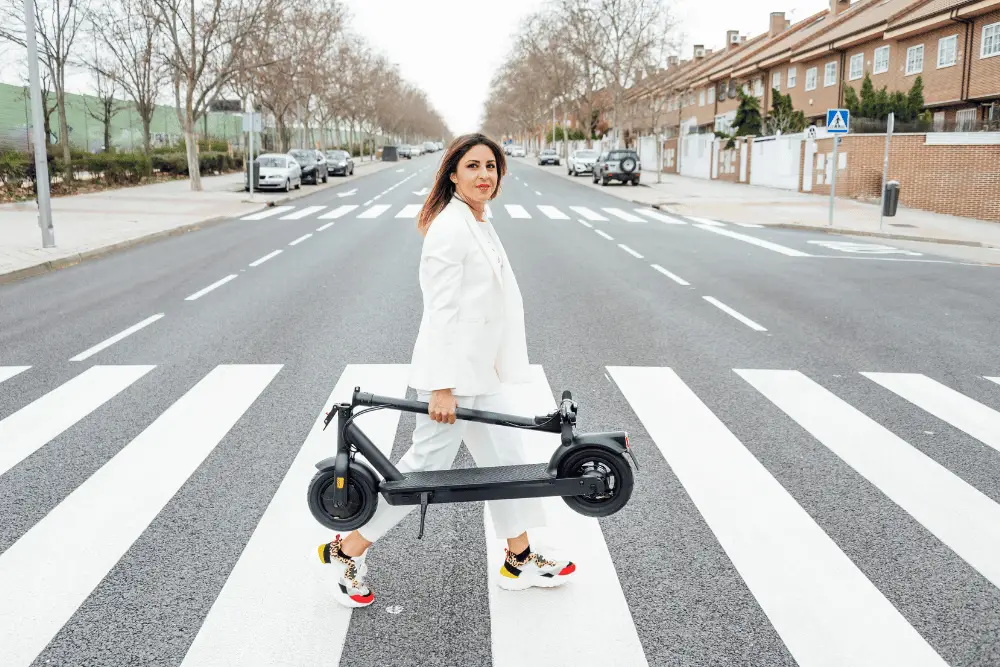 A female in white dress carrying an electric scooter by hand