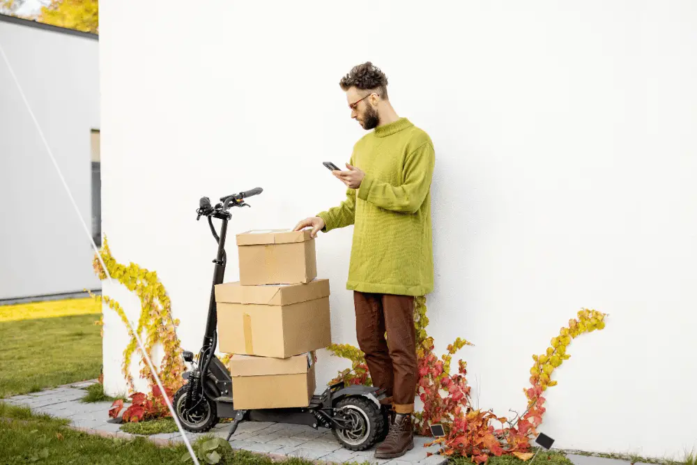 A man standing beside its electric scooter having boxes on it