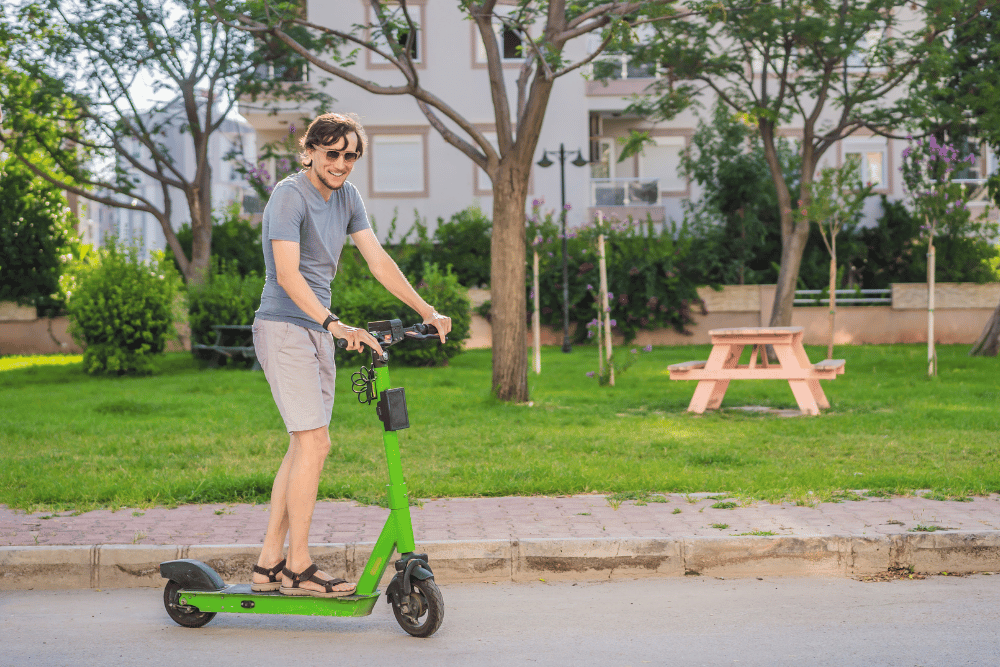A guy in grey t-shirt and short riding an electric scooter