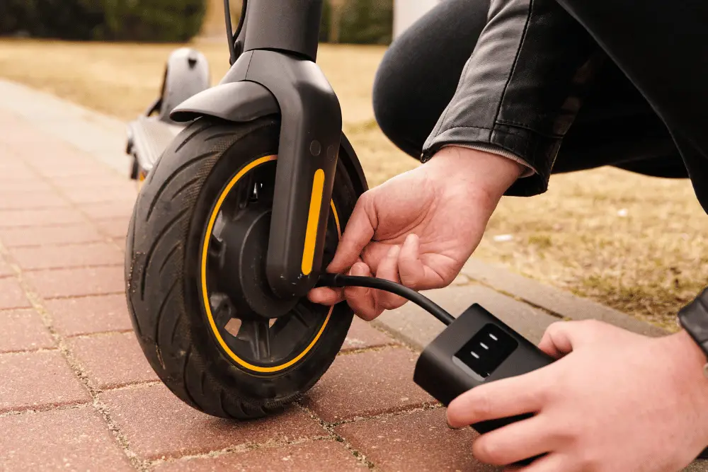 A person filling a tire of an electric scooter using portable air pump