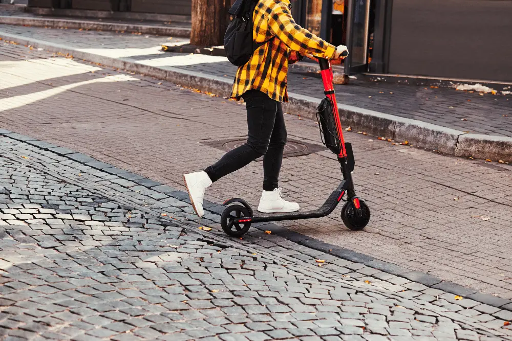 A person with black and red electric scooter on a street