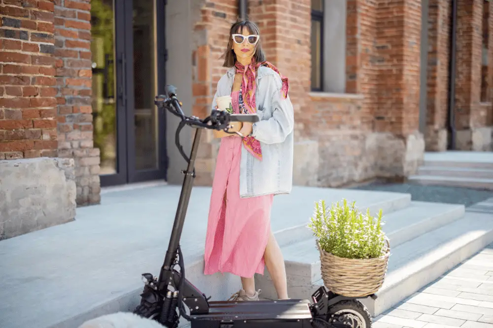 A lady in pink dress and glasses standing with black electric scooter