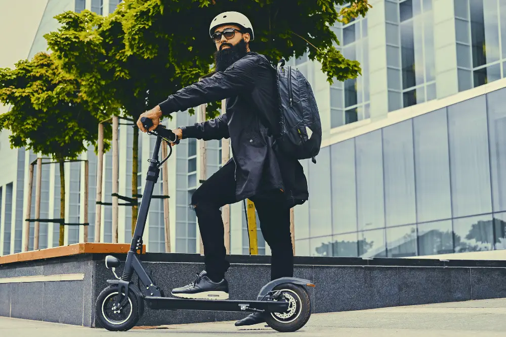 A beard man wearing glasses, hamlet, and bag pack on electric scooter 