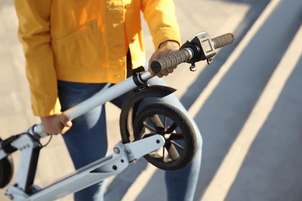 A person with yellow shirt and tight jeans holding an electric scooter