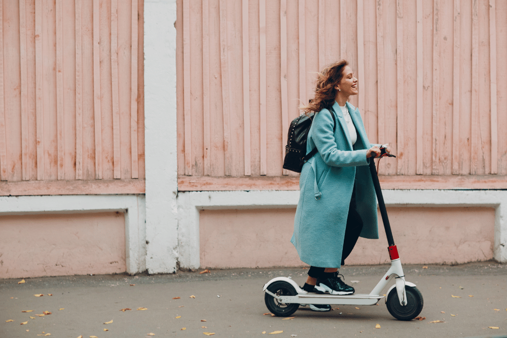 A lady in a log coat riding an electric scooter
